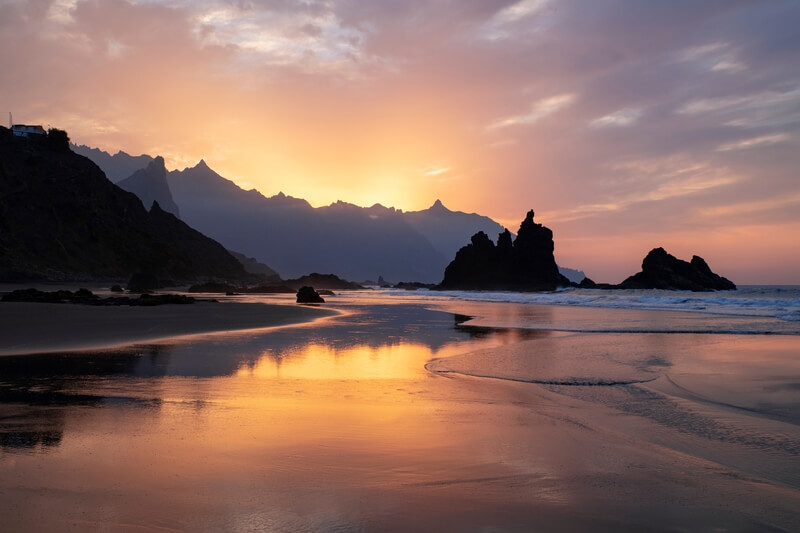 Coucher de soleil sur la plage de Benijo, au nord de Tenerife, avec des formations rocheuses volcaniques se reflétant dans l'eau.